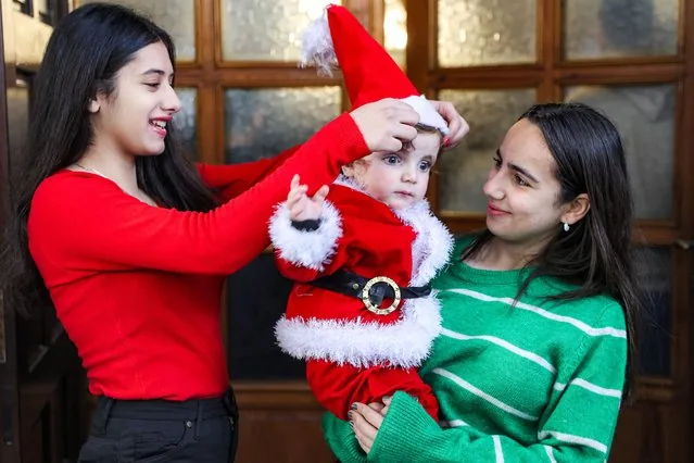 Girl places Santa hat on child outside Saint Porphyrius Church Gaza City January 2025